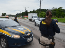 Policial de costas ao lado do carro da PRF na rodovia