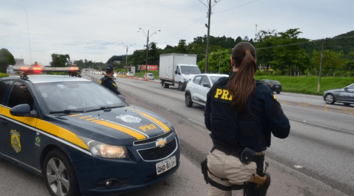 Policial de costas ao lado do carro da PRF na rodovia