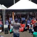 Servidores da Comcap encerram greve em assembleia - grupo com os braços para cima debaixo de tendas; homem à frente no microfone