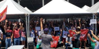 Servidores da Comcap encerram greve em assembleia - grupo com os braços para cima debaixo de tendas; homem à frente no microfone