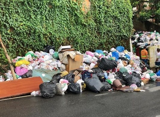 Coleta seletiva será retomada na quarta em Florianópolis montanha de sacos de lixo acumulada em calçada com dois funcionários ao lado - Coleta seletiva será retomada na quarta em Florianópolis