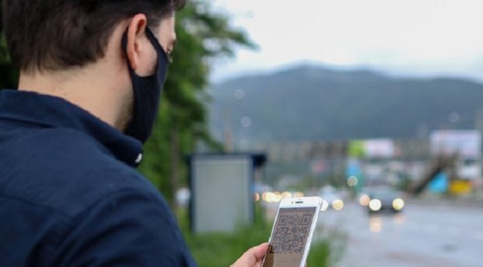 Homem com máscara visto de trás com o celular que mostra um QR Code, que é uma das alternativas de pagamento do bilhete digital em Santa Catarina