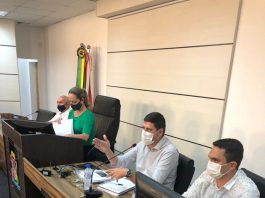 Sentados lado a lado em uma mesa com computadores, os secretários de São José falam sobre invasões de terra no município. Ao lado deles, também lado a lado, outras duas pessoas com máscara.