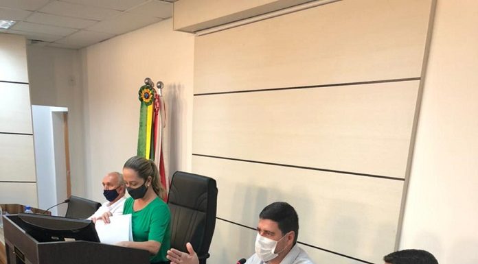 Sentados lado a lado em uma mesa com computadores, os secretários de São José falam sobre invasões de terra no município. Ao lado deles, também lado a lado, outras duas pessoas com máscara.