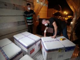 Dois homens com máscaras com três caixotes contendo as doses da vacina contra a Covid-19