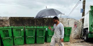 homem passa com guarda-chuva em frente a contentores de lixo vazios em região do continente de Florianópolis