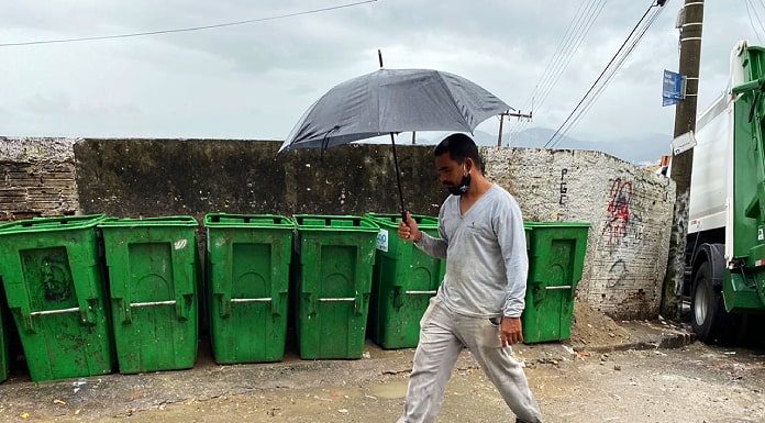 homem passa com guarda-chuva em frente a contentores de lixo vazios em região do continente de Florianópolis