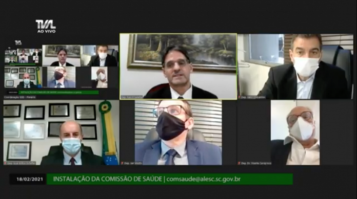 Captura de tela de reunião com deputados da Comissão da Saúde da Alesc. Na imagem, seis telas, a primeira uma versão menor da da imagem completa e nas outras telas os deputados.