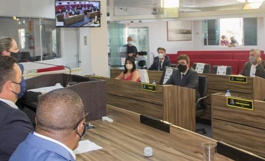 vereadores sentados na mesa diretora e nas bancadas, todos usando máscara, na sessão de criação da comissão