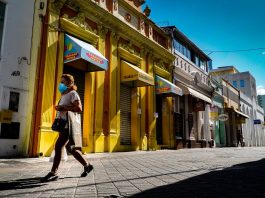 Quais serviços fecham no fim de semana com o novo decreto estadual Serviços não essenciais: mulher de máscara caminha em frente ao comércio fechado do centro de florianópolisq