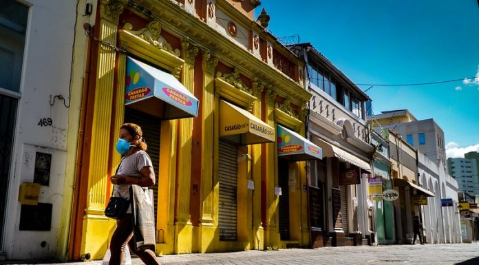Serviços não essenciais: mulher de máscara caminha em frente ao comércio fechado do centro de florianópolisq
