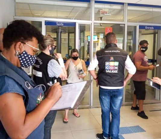 fiscais do procon usando coletes e fazendo anotações em hall de banco - Demora no atendimento de bancos motiva fiscalização do Procon em São José