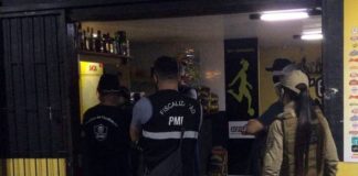 São José e Florianópolis: policial mulher ao lado de fiscais da prefeitura na entrada de um bar; todos vistos de costas