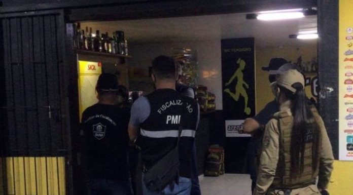 São José e Florianópolis: policial mulher ao lado de fiscais da prefeitura na entrada de um bar; todos vistos de costas