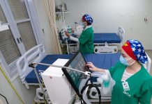 duas profissionais de saúde mexem em equipamentos de uti com leitos vazios - governo suspende consultas e exames para desafogar hospitais
