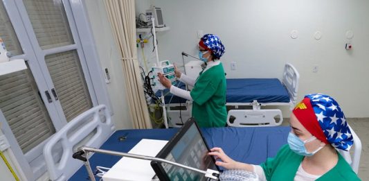duas profissionais de saúde mexem em equipamentos de uti com leitos vazios - governo suspende consultas e exames para desafogar hospitais