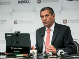 Deputado Julio Garcia tem pele branca e cabelo escuro penteado para trás, usa terno escuro com gravata vermelha, está a frente de microfones em cima de uma mesa e tem a sua frente também um computador e uma placa com seu nome, atrás um banner com logo da Alesc e rádio AL. Nesta semana o STF julgou a reclamação da Alesc procedente e Julio Garcia poderá retornar ao cargo.