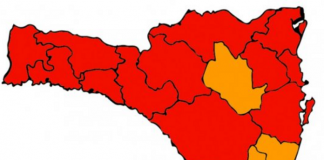 Desenho do mapa de Santa Catarina com 16 divisões de regiões, sendo quatro em cor laranja e dez em cor vermelha. O mapa representa a nova matriz de risco à Covid-19 do estado.