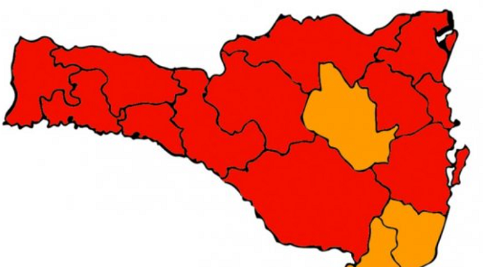 Desenho do mapa de Santa Catarina com 16 divisões de regiões, sendo quatro em cor laranja e dez em cor vermelha. O mapa representa a nova matriz de risco à Covid-19 do estado.