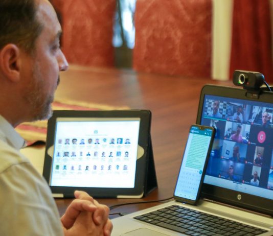 moisés em frente a dois computadores em webconferência com prefeitos sobre novas medidas para conter coronavírus