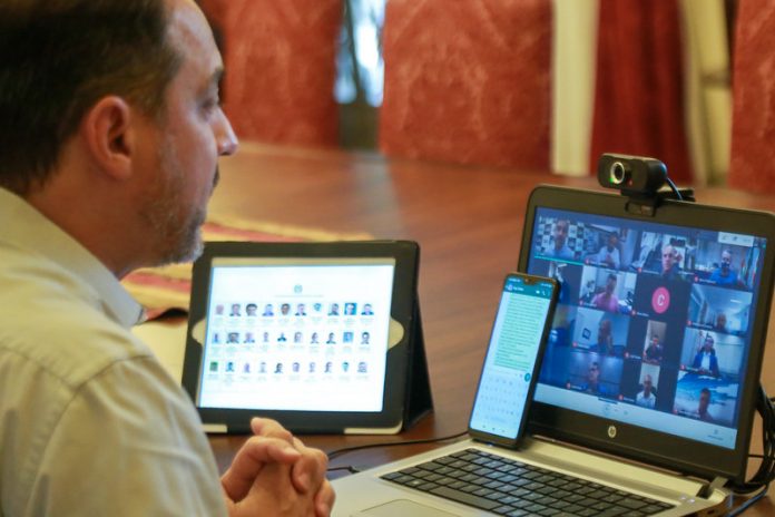 moisés em frente a dois computadores em webconferência com prefeitos sobre novas medidas para conter coronavírus