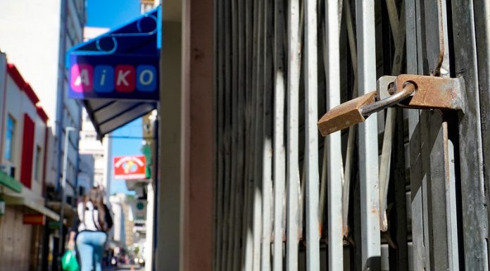 cadeado fechando loja no centro de florianópolis e mulher passando ao fundo em calçadão - orgãos recomendam lockdown em sc