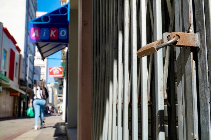 cadeado fechando loja no centro de florianópolis e mulher passando ao fundo em calçadão - orgãos recomendam lockdown em sc