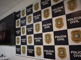 Técnico de enfermagem é preso por suspeita de estupro de paciente A imagem ilustra a prisão efetuado por policiais civis de um homem suspeito de estupro em São José. Painel com quadros brancos e brasão da polícia civil ao lado de quadros pretos com a escrita em branco de "polícia civil". Ao lado há um televisor.
