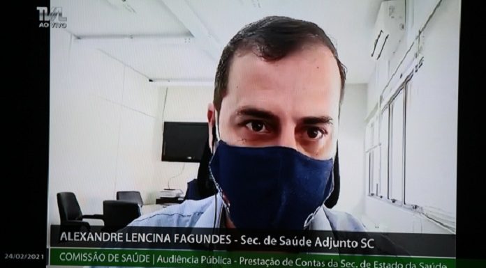Foto de uma tela em que aparece o secretário de saúde adjunto em audiência pública na Alesc. Ele é branco e tem cabelo curto e escuro. Usa máscara cobrindo nariz e boca.