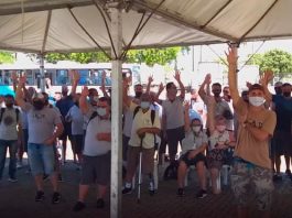 funcionários do transporte coletivo da grande florianópolis reunidos sob tenda com os braços levantados; todos usam máscaras