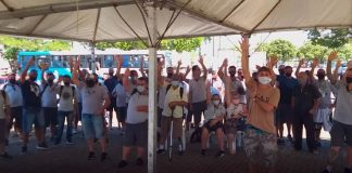 funcionários do transporte coletivo da grande florianópolis reunidos sob tenda com os braços levantados; todos usam máscaras