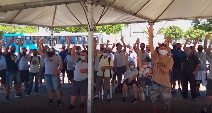 funcionários do transporte coletivo da grande florianópolis reunidos sob tenda com os braços levantados; todos usam máscaras