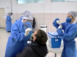 casos ativos por bairros de coronavírus em florianópolis - profissional de saúde usando epi se inclina para fazer teste com cotonete no nariz de homem com cabeça inclinada para trás