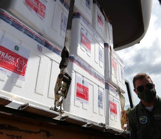 caixas de isopor com as doses de vacina; adesivos na parte externa com desenho do zé gotinha; militar da aeronáutica ao lado com máscara e óculos escuro