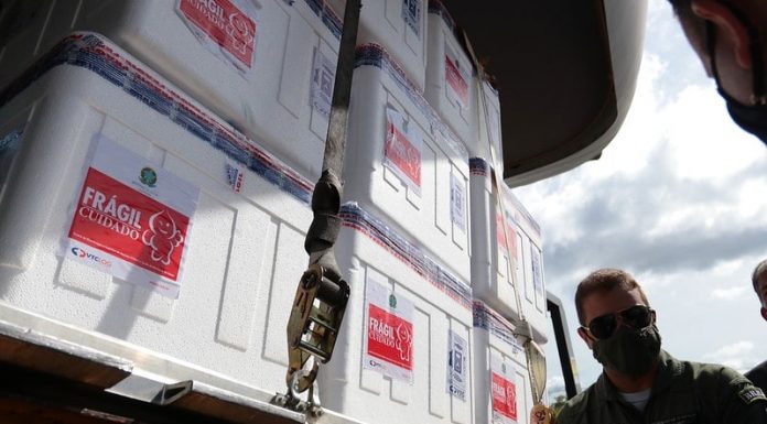 caixas de isopor com as doses de vacina; adesivos na parte externa com desenho do zé gotinha; militar da aeronáutica ao lado com máscara e óculos escuro