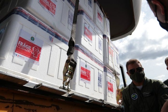 caixas de isopor com as doses de vacina; adesivos na parte externa com desenho do zé gotinha; militar da aeronáutica ao lado com máscara e óculos escuro