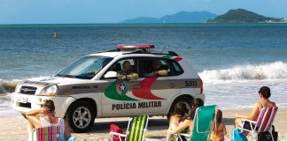viatura suv da polícia passando por pessoas sentadas na areia da praia
