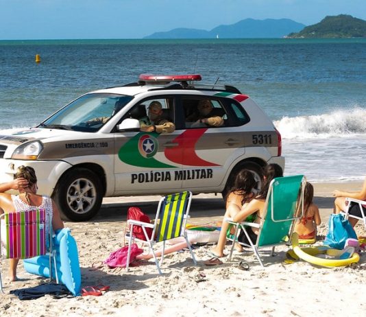 viatura suv da polícia passando por pessoas sentadas na areia da praia