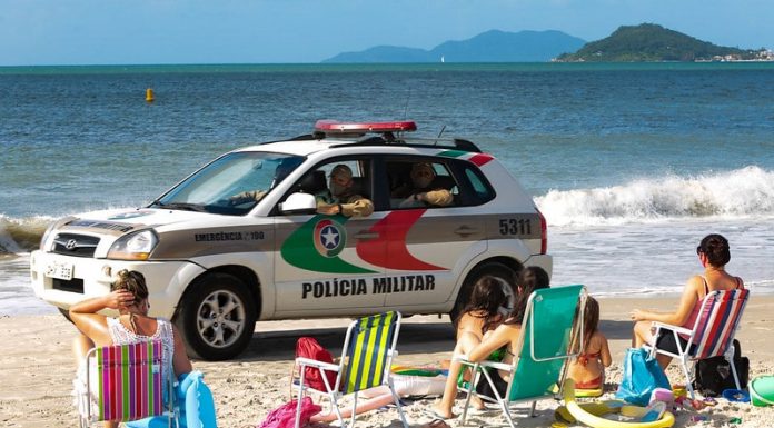 viatura suv da polícia passando por pessoas sentadas na areia da praia