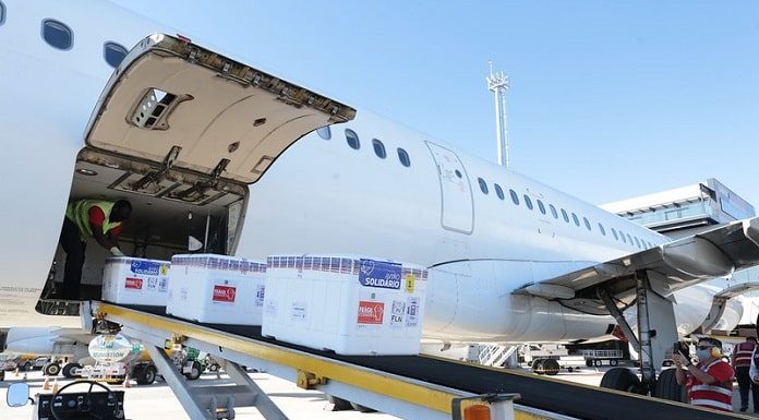 três caixas de isopor com as doses de vacina saem de esteira de avição