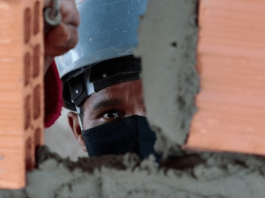 Empregos do Sine para a Grande Florianópolis: Homem com capacete e máscara, construindo uma parede com tijolos e cimento