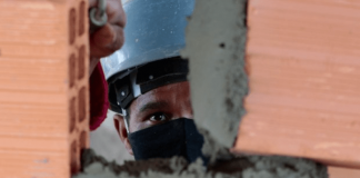 Empregos do Sine para a Grande Florianópolis: Homem com capacete e máscara, construindo uma parede com tijolos e cimento