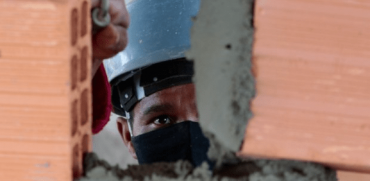 Empregos do Sine para a Grande Florianópolis: Homem com capacete e máscara, construindo uma parede com tijolos e cimento