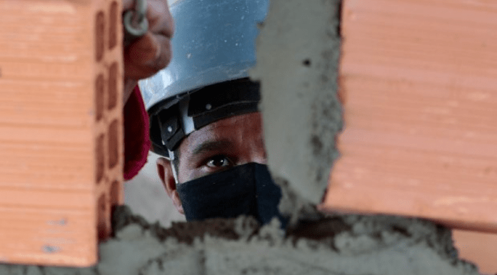 Empregos do Sine para a Grande Florianópolis: Homem com capacete e máscara, construindo uma parede com tijolos e cimento