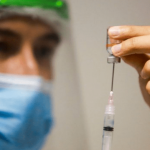 Santa Catarina tem 323 mil doses aplicadas contra Covid-19: Profissional da saúde, equipado com EPI, colocando a vacina na seringa