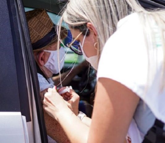 profissional de saúde aplica vacina no braço de idoso dentro de carro - Vacinação contra Covid em idosos a partir de 78 anos tem início em Palhoça