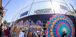 grafiteiros pintando parede de quadra de esportes com uso de escadas