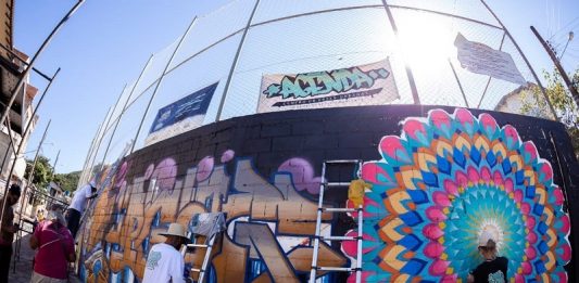 grafiteiros pintando parede de quadra de esportes com uso de escadas