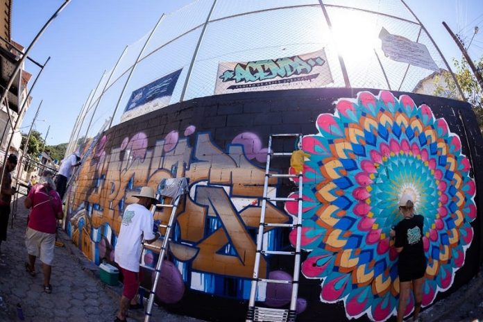 grafiteiros pintando parede de quadra de esportes com uso de escadas
