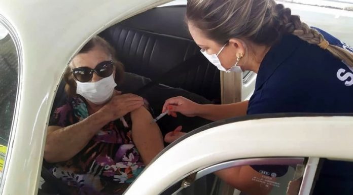 idosa usando máscara e óculos escuro é vacinada por profissional de saúde dentro de um fusca